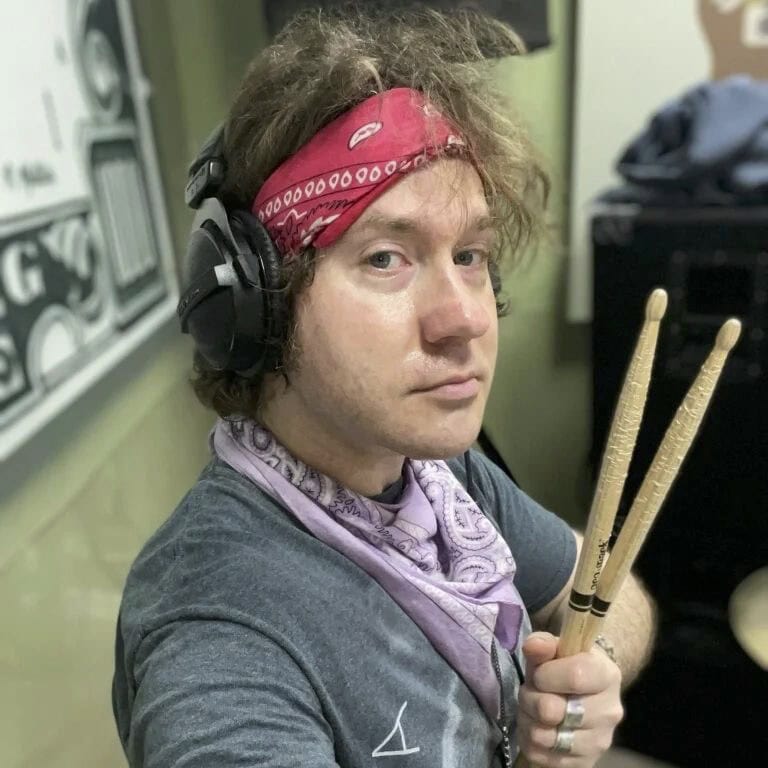 Martin wearing headphones and a red bandana holding a set of drumsticks.