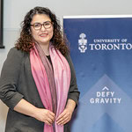 A woman in a pink scarf posing in front of a U of T banner.