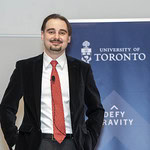 A man in a business suit posing in front of a U of T banner.