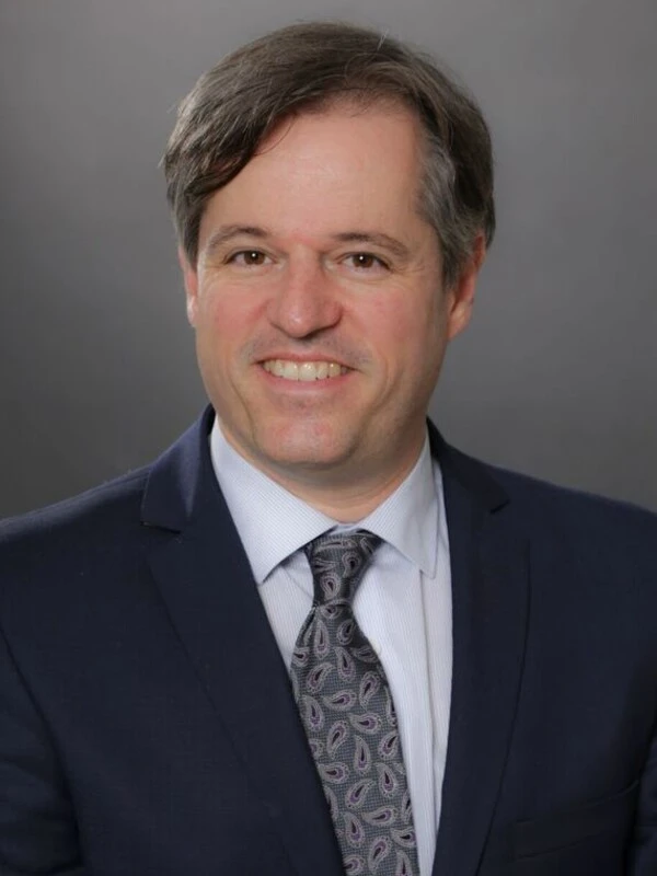 A formal headshot of a man in a business suit smiling.