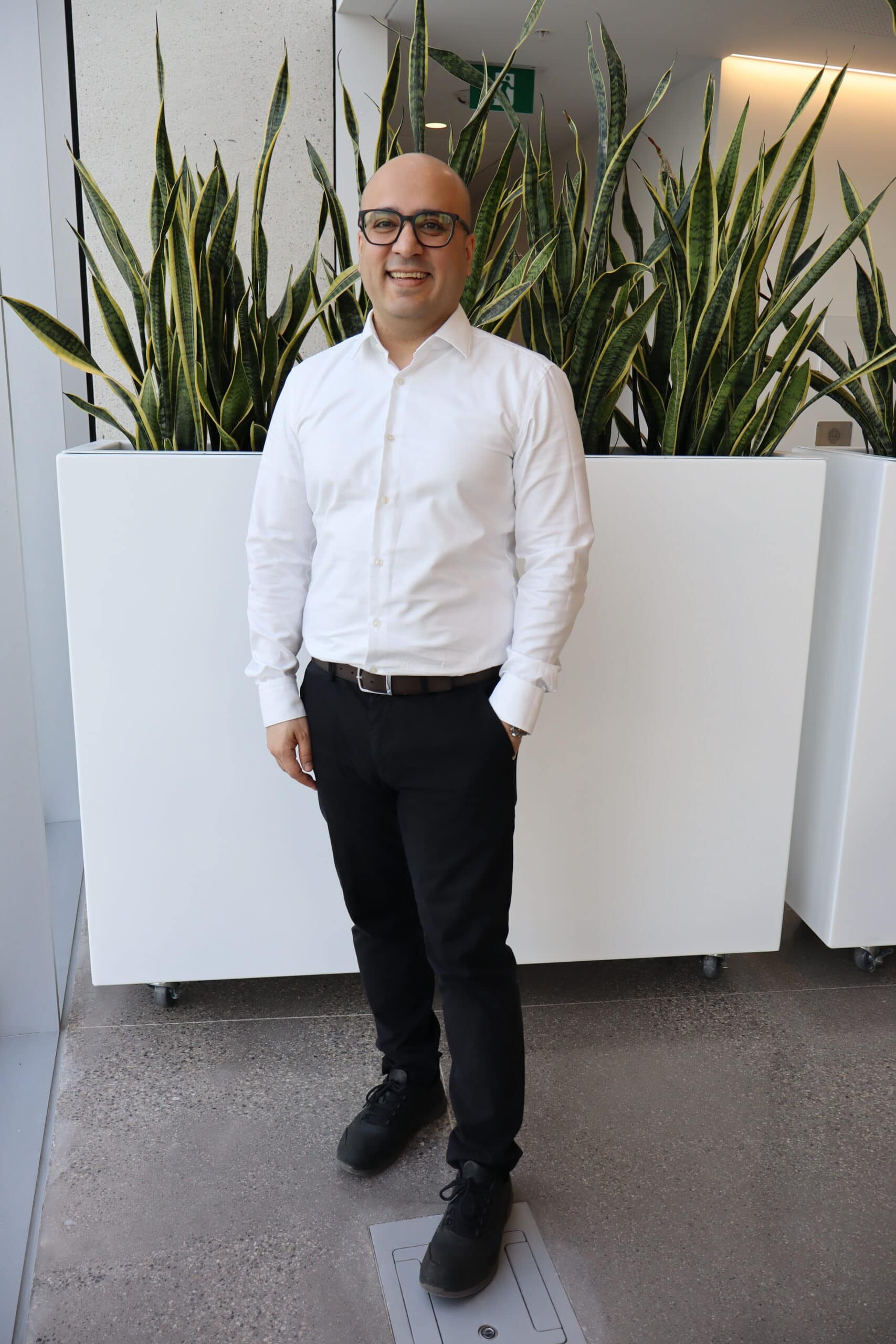 A person in smart-casual attired standing in front of some potted plants