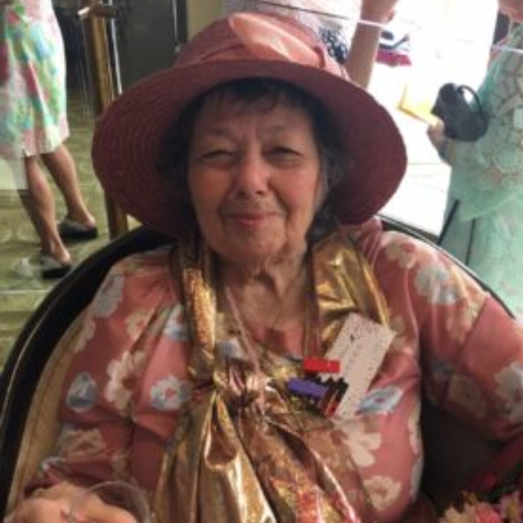 A seated woman smiles. She is wearing a pink hat and top. 