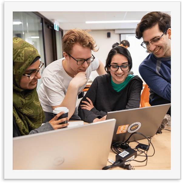Group of Engineering students gathered around computer desks doing group work